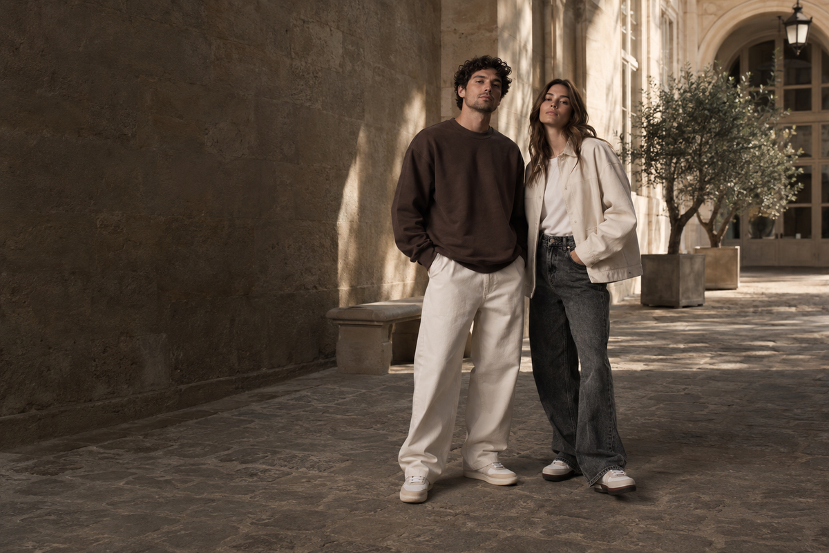 Deux silhouettes streetwear dans une cour en pierre, tons bruns et écrus.
